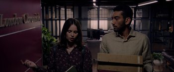 Movie still from “The Last Letter from Your Lover” (2021), directed by Augustine Frizzell – A woman and a man standing next to each other in an office; Medium shot, Over the shoulder angle