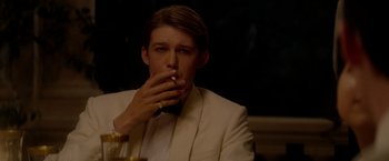 Movie still from “The Last Letter from Your Lover” (2021), directed by Augustine Frizzell – A man sitting at a table with a cigarette in his mouth; Close Up shot, Over the shoulder angle