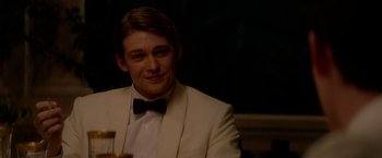 Movie still from “The Last Letter from Your Lover” (2021), directed by Augustine Frizzell – A man in a white suit sitting at a table; Close Up shot, Over the shoulder angle