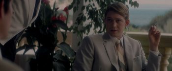 Movie still from “The Last Letter from Your Lover” (2021), directed by Augustine Frizzell – A man wearing a suit and tie in front of a plant; Medium shot, Over the shoulder angle