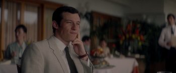 Movie still from “The Last Letter from Your Lover” (2021), directed by Augustine Frizzell – A man wearing a suit and tie sitting at a table; Close Up shot, Over the shoulder angle