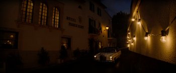 Movie still from “The Last Letter from Your Lover” (2021), directed by Augustine Frizzell – A car parked in front of a building at night; Extreme Wide shot, Low angle