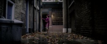 Movie still from “The Last Letter from Your Lover” (2021), directed by Augustine Frizzell – A woman in a purple dress walking down a street; Wide shot, High angle