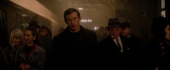 Movie still from “The Last Letter from Your Lover” (2021), directed by Augustine Frizzell – A man standing next to another man wearing a hat; Medium shot, Low angle