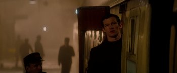 Movie still from “The Last Letter from Your Lover” (2021), directed by Augustine Frizzell – A man standing next to a wall in a dark room; Medium shot, Over the shoulder angle