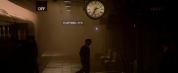 Movie still from “The Last Letter from Your Lover” (2021), directed by Augustine Frizzell – A man walking in a train station next to a clock; Extreme Wide shot, High angle