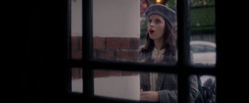 Movie still from “The Last Letter from Your Lover” (2021), directed by Augustine Frizzell – A woman wearing a hat and a jacket looking out of a window; Medium shot, Over the shoulder angle