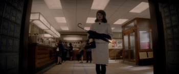 Movie still from “The Last Letter from Your Lover” (2021), directed by Augustine Frizzell – A woman holding an umbrella in an office building; Medium shot, Low angle