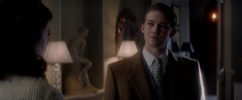 Movie still from “The Last Letter from Your Lover” (2021), directed by Augustine Frizzell – A man wearing a suit and tie standing in front of a statue; Medium shot, Over the shoulder angle