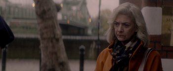 Movie still from “The Last Letter from Your Lover” (2021), directed by Augustine Frizzell – An older woman wearing an orange coat standing in front of a tree; Close Up shot, Over the shoulder angle