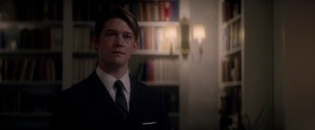 Movie still from “The Last Letter from Your Lover” (2021), directed by Augustine Frizzell – A man in a suit and tie in front of a bookshelf; Close Up shot, Over the shoulder angle