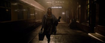 Movie still from “The Last Letter from Your Lover” (2021), directed by Augustine Frizzell – A woman walking down a train platform holding a suitcase; Wide shot, High angle