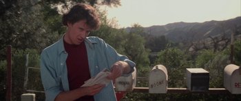 Movie still from “The Last Starfighter” (1984), directed by Nick Castle – A young man holding a piece of paper near two mailboxes; Close Up shot, Over the shoulder angle