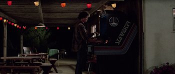Movie still from “The Last Starfighter” (1984), directed by Nick Castle – A man playing a video game in a room; Wide shot, Low angle