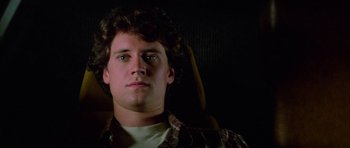 Movie still from “The Last Starfighter” (1984), directed by Nick Castle – A young man sitting in a car seat looking into the camera; Close Up shot, Low angle