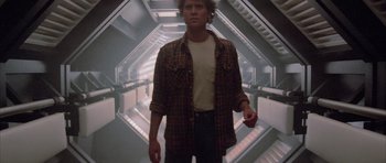 Movie still from “The Last Starfighter” (1984), directed by Nick Castle – A man standing in a hallway with stairs in the background; Medium shot, Low angle
