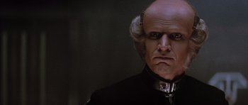 Movie still from “The Last Starfighter” (1984), directed by Nick Castle – A man with a bald head wearing a black suit; Close Up shot, Low angle