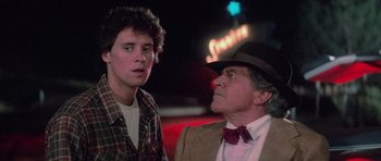 Movie still from “The Last Starfighter” (1984), directed by Nick Castle – A man and a young boy standing next to each other in front of a neon sign at night; Close Up shot, Over the shoulder angle