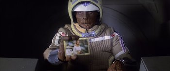 Movie still from “The Last Starfighter” (1984), directed by Nick Castle – A person in a spacesuit holding a picture of jesus; Close Up shot, Over the shoulder angle