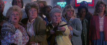 Movie still from “The Last Starfighter” (1984), directed by Nick Castle – A group of people standing in front of each other holding a remote; Medium shot, Low angle