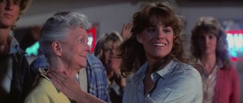 Movie still from “The Last Starfighter” (1984), directed by Nick Castle – A woman smiles at a crowd of people in a room; Close Up shot, Over the shoulder angle