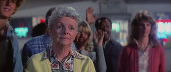 Movie still from “The Last Starfighter” (1984), directed by Nick Castle – An older woman is standing in front of a group of people; Close Up shot, Over the shoulder angle