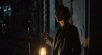 Movie still from “The Last Vermeer” (2019), directed by Dan Friedkin – A woman holding a lantern in the dark outside; Medium shot, Low angle