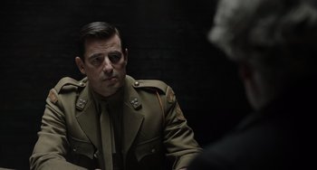 Movie still from “The Last Vermeer” (2019), directed by Dan Friedkin – A man in a military uniform sitting in front of a woman; Medium shot, Over the shoulder angle