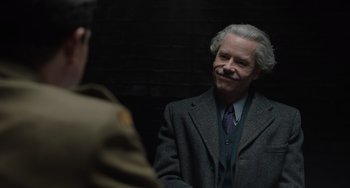 Movie still from “The Last Vermeer” (2019), directed by Dan Friedkin – An older man wearing a suit and tie; Close Up shot, Over the shoulder angle