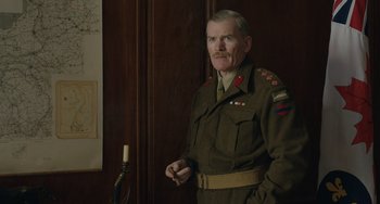 Movie still from “The Last Vermeer” (2019), directed by Dan Friedkin – An older man in a uniform standing in front of a wall; Medium shot, Low angle
