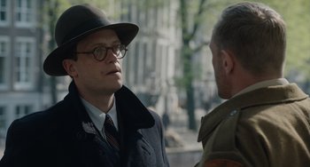 Movie still from “The Last Vermeer” (2019), directed by Dan Friedkin – A man wearing a hat and glasses talking to another man; Close Up shot, Over the shoulder angle
