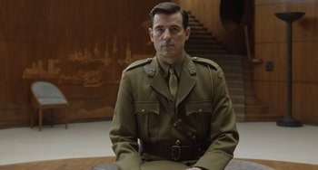 Movie still from “The Last Vermeer” (2019), directed by Dan Friedkin – A man in a uniform sitting on the ground; Medium shot, Over the shoulder angle