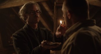 Movie still from “The Last Vermeer” (2019), directed by Dan Friedkin – An older man lighting a candle for a younger man; Medium shot, Low angle