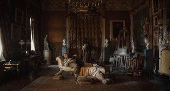 Movie still from “The Last Vermeer” (2019), directed by Dan Friedkin – A man sitting in a chair next to a statue; Wide shot, Low angle