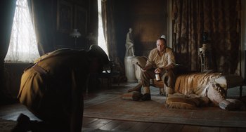 Movie still from “The Last Vermeer” (2019), directed by Dan Friedkin – A man sitting on the floor reading a magazine; Wide shot, Low angle