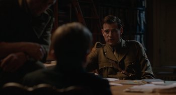 Movie still from “The Last Vermeer” (2019), directed by Dan Friedkin – A man in a military uniform sitting at a table; Medium shot, Over the shoulder angle
