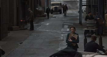Movie still from “The Last Vermeer” (2019), directed by Dan Friedkin – A woman walking down a street holding a book; Wide shot, High angle