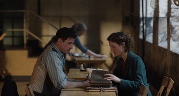 Movie still from “The Last Vermeer” (2019), directed by Dan Friedkin – A man and a woman sitting at a wooden table; Medium shot, Over the shoulder angle