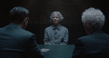 Movie still from “The Last Vermeer” (2019), directed by Dan Friedkin – A man sitting at a table in front of two other men; Medium shot, Over the shoulder angle