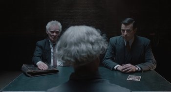 Movie still from “The Last Vermeer” (2019), directed by Dan Friedkin – Two men sitting at a table in front of another man; Medium shot, Over the shoulder angle