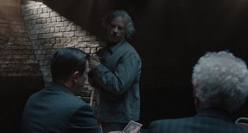 Movie still from “The Last Vermeer” (2019), directed by Dan Friedkin – A man in a gray jacket standing next to another man in a gray jacket; Medium shot, Over the shoulder angle