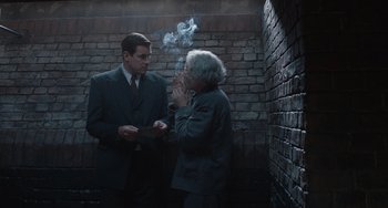 Movie still from “The Last Vermeer” (2019), directed by Dan Friedkin – Two men standing in a dark room with smoke coming out of their mouths; Medium shot, Over the shoulder angle