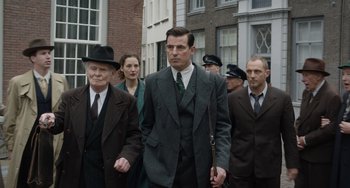 Movie still from “The Last Vermeer” (2019), directed by Dan Friedkin – A group of men in suits and ties walking down a street; Medium shot, Over the shoulder angle