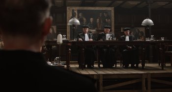 Movie still from “The Last Vermeer” (2019), directed by Dan Friedkin – A group of men sitting at a table in front of a painting; Wide shot, Over the shoulder angle
