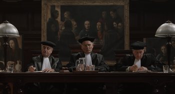 Movie still from “The Last Vermeer” (2019), directed by Dan Friedkin – Three judges sitting at a table in front of a painting; Wide shot, Low angle