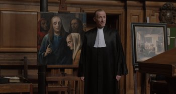 Movie still from “The Last Vermeer” (2019), directed by Dan Friedkin – A man dressed as a priest standing in front of a painting; Medium shot, Over the shoulder angle