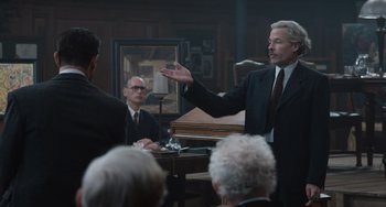 Movie still from “The Last Vermeer” (2019), directed by Dan Friedkin – An older man in a suit and tie talking to a group; Medium shot, Over the shoulder angle