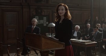 Movie still from “The Last Vermeer” (2019), directed by Dan Friedkin – A woman standing at a podium in front of judges; Medium shot, Over the shoulder angle