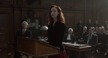 Movie still from “The Last Vermeer” (2019), directed by Dan Friedkin – A woman standing at a podium in a court room; Medium shot, Over the shoulder angle