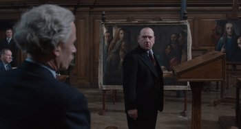 Movie still from “The Last Vermeer” (2019), directed by Dan Friedkin – A man standing in front of a painting in a room; Medium shot, Over the shoulder angle